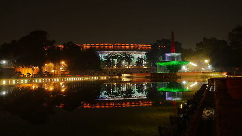 Illuminated buildings by river against sky at night