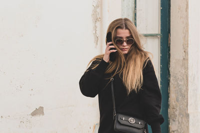 Young woman wearing sunglasses standing against wall