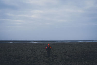 Rear view of man standing on field against sky