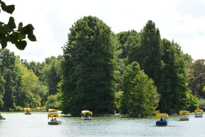 Boats in river by trees against sky