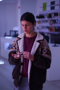 Young woman putting bandage on finger while standing at home