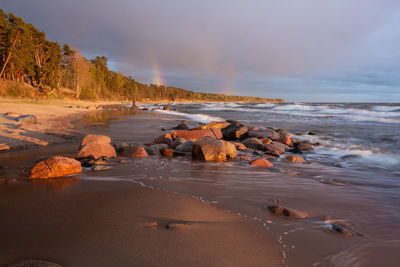 Rocks on beach against sky during sunset