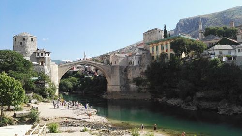 People at riverbank against clear sky