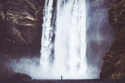 Woman with arms outstretched standing by waterfall 