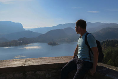 Man sitting by lake against sky