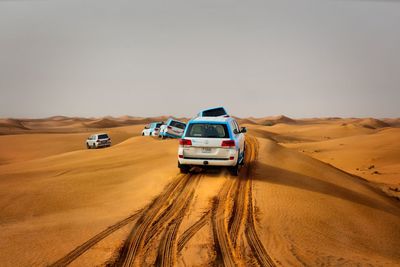 Cars on sand dune in desert against sky