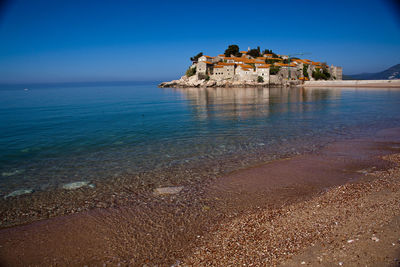 Scenic view of sea by buildings against clear blue sky