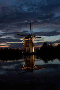 Traditional windmill by lake against sky during sunset