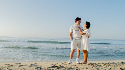 Young couple standing on beach against clear sky