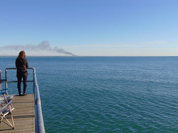 Rear view of woman standing on pier over sea