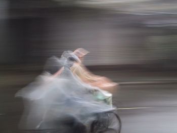 Blurred motion of person wearing raincoat while cycling on street