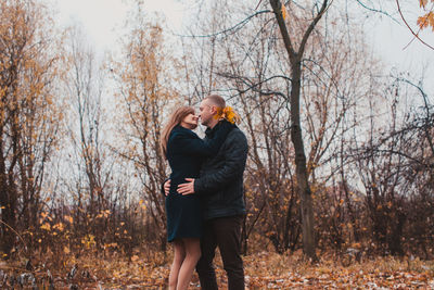 Full length of woman standing by bare trees in forest