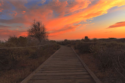 Boardwalk against cloudy sky during sunset