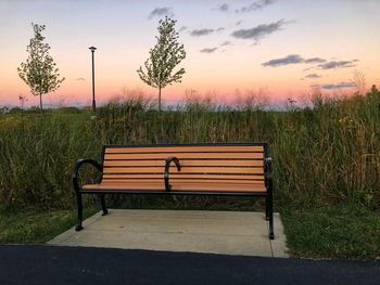 Empty bench on field against sky during sunset