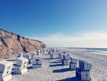 Hooded chairs at beach against sky on sunny day