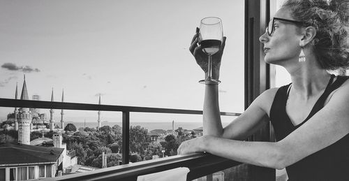 Young woman looking away by railing against window