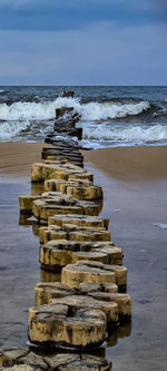 Stack of wooden post on beach against sky