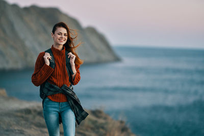 Portrait of smiling young woman standing on sea shore against sky