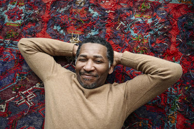 Smiling mature man with hands behind head lying on carpet