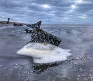 Sea waves splashing on shore at beach against sky