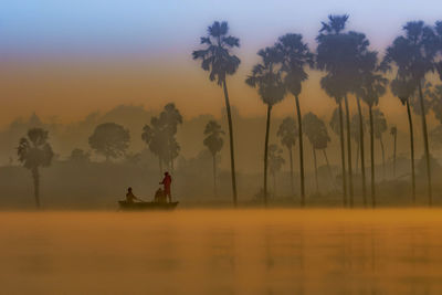 Silhouette trees by lake against sky during sunset