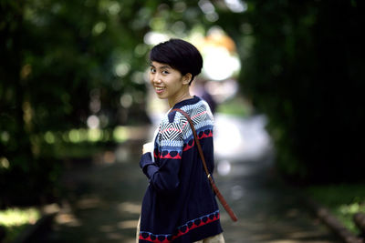 Portrait of happy woman standing on footpath at park