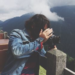 Photographer photographing through camera while leaning on railing