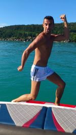 Portrait of shirtless man flexing muscles in boat on sea
