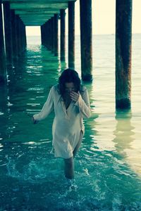 Young woman walking on sea shore below pier