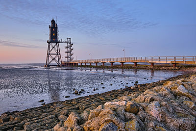 Lighthouse by sea against sky during sunset