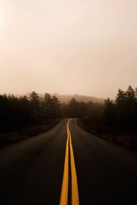 View of country road along trees against clear sky