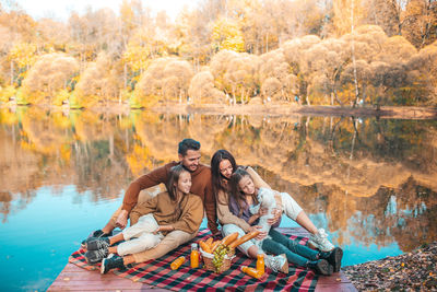 Cheerful family sitting on pier by lake at forest