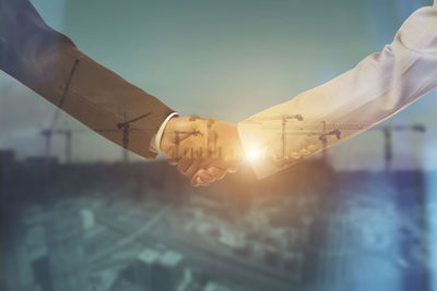 Double exposure of businessman and businesswoman shaking hands against cityscape