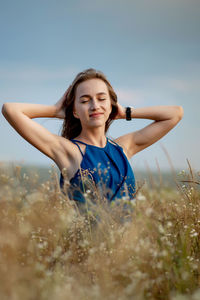 Young woman with arms raised on field against sky