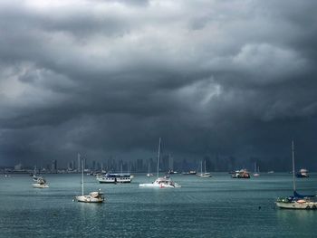 Sailboats in sea against storm clouds