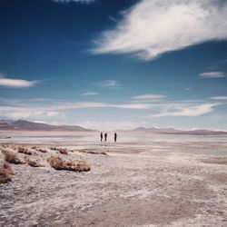 People standing at distance on land against cloudy sky