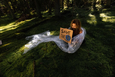 Girl holding a cardboard tablet in hand. the girl is wrapped in plastic film and lies on the ground