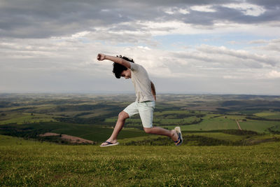 Boy jumping over land against cloudy sky