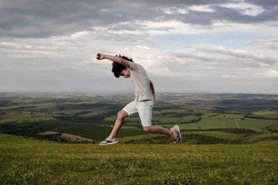 Man walking on grassy field against cloudy sky