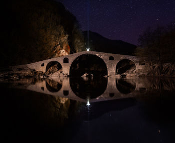 Illuminated bridge over river against sky at night