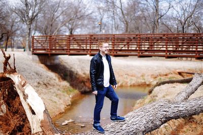 Full length of man standing on tree trunk against bridge