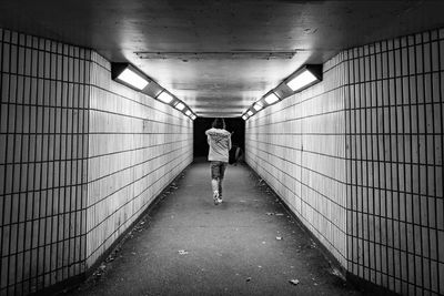 Rear view of man walking in illuminated tunnel