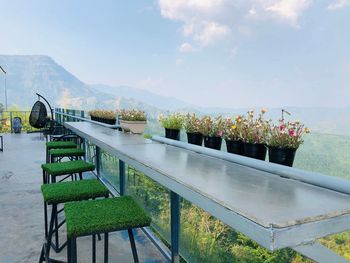 Empty chairs and table by potted plants against sky
