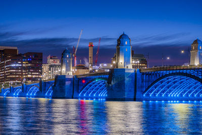 Illuminated bridge over river in city at night