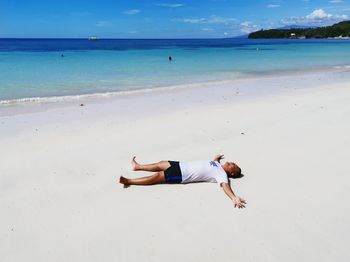 Man relaxing on sand at beach against sky