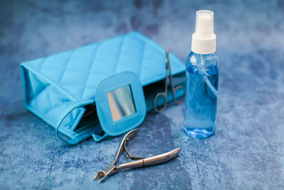 Close-up of small spray bottle with clutch bag and tweezers on blue table