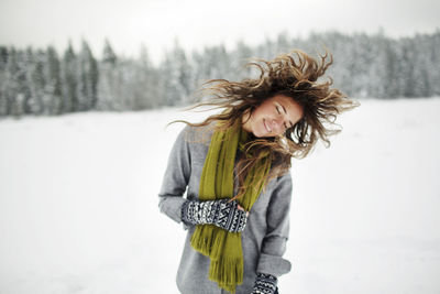 Happy woman tossing hair while standing on snow covered field in forest