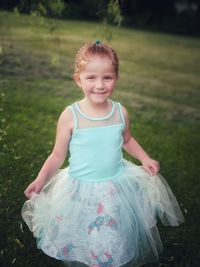 Portrait of cute smiling girl wearing blue dress while standing on field