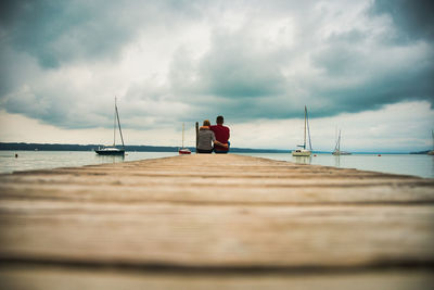 Rear view of people sitting on pier against sky