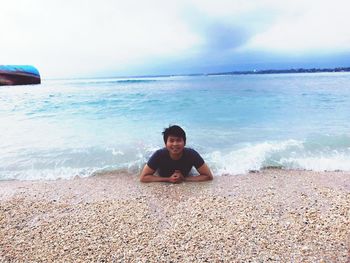 Portrait of young man lying at seashore against sky